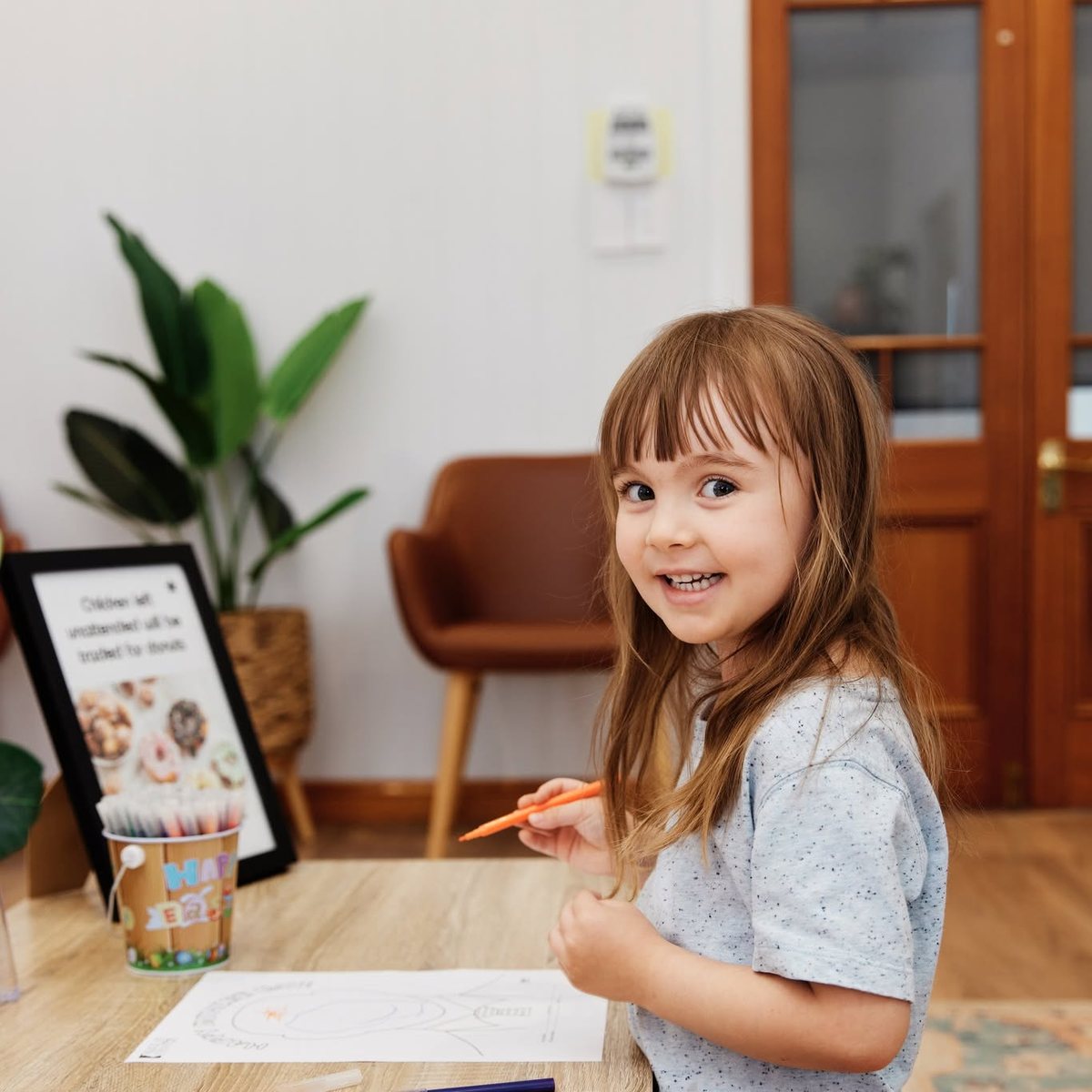 A young girl smiling while colouring in at the children's table in the waiting lounge