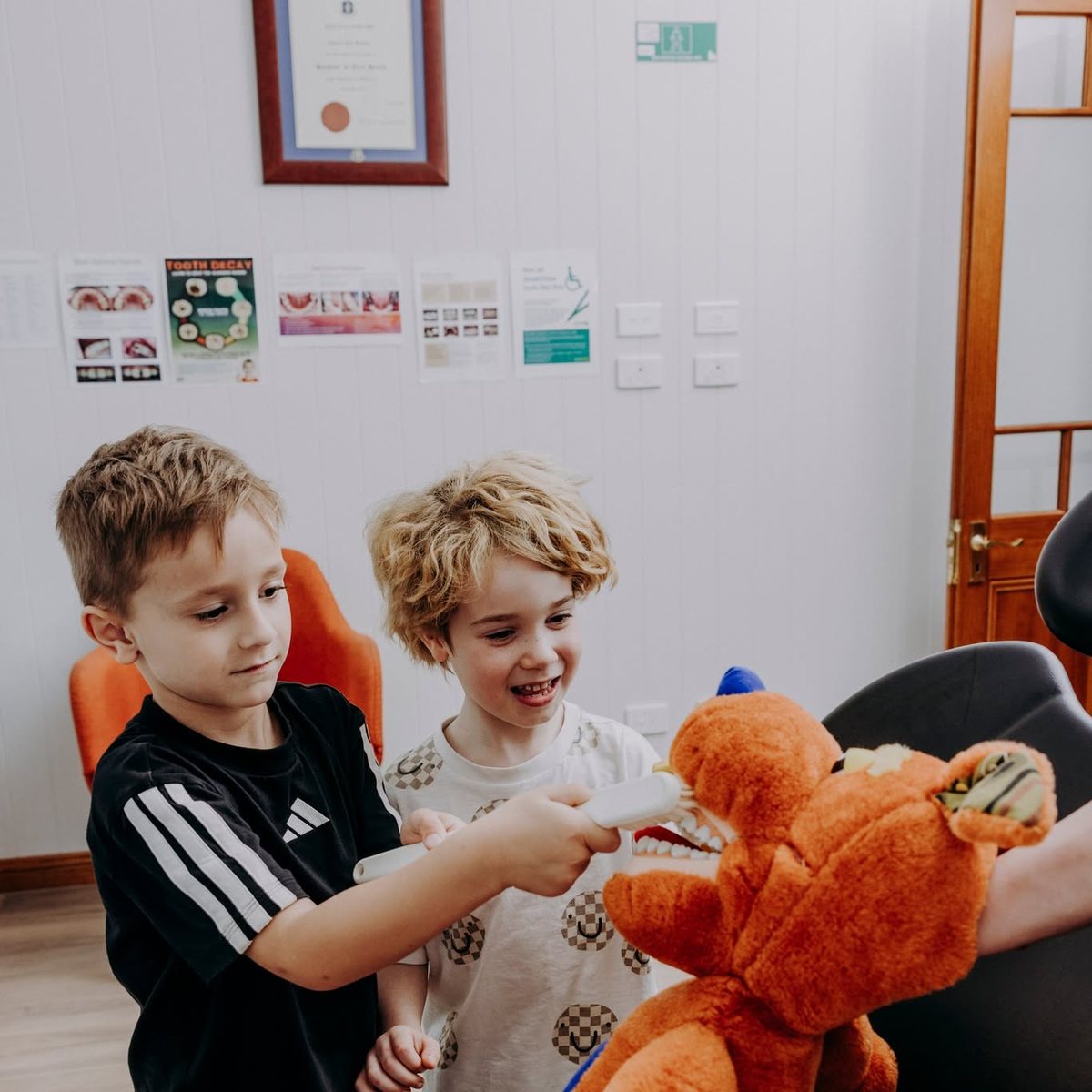 Two children practising brushing on a toy bear at the practice